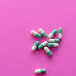 A small pile of over-the-counter pain relievers on a pink background.