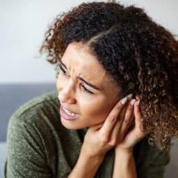 Woman with tinnitus pressing her hand to her ear.