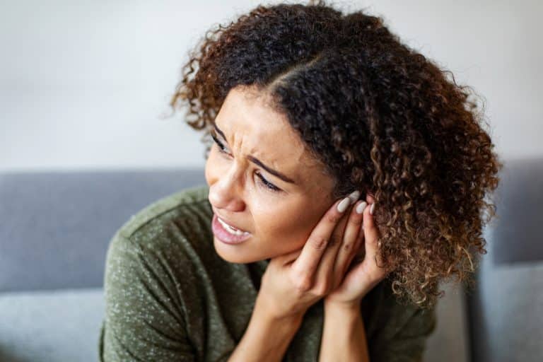 Woman with tinnitus pressing her hand to her ear.