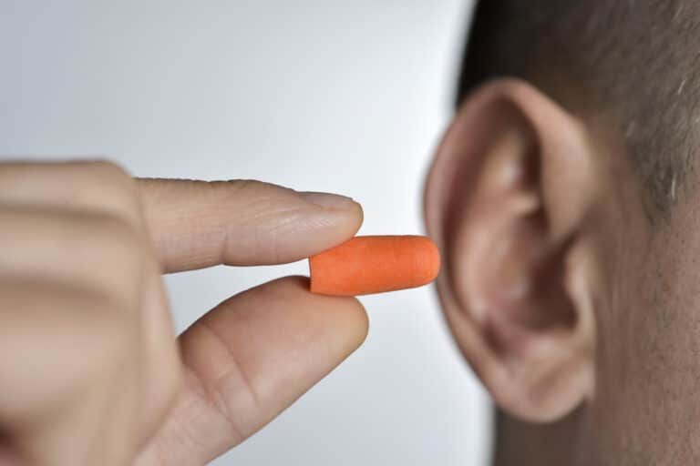 Man putting an earplug into his ear for hearing protection.