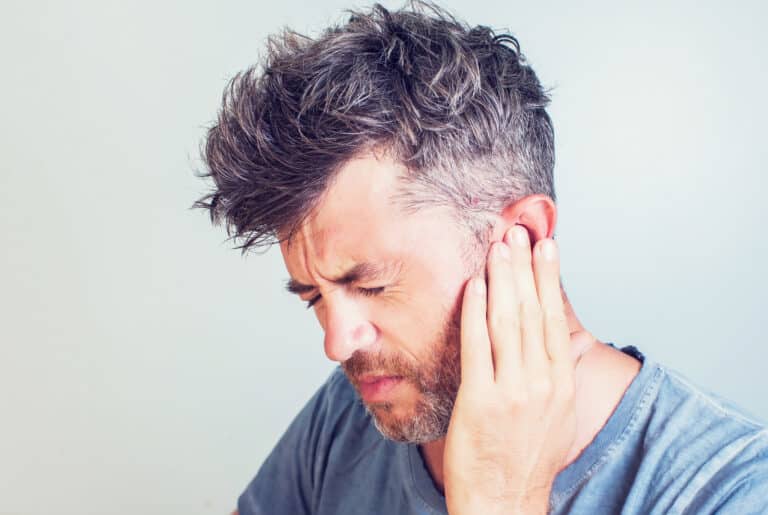Man with tinnitus pressing his ringing ear.