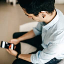 Younger businessman with a hearing aid looks at his smartphone.