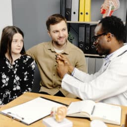 Audiologist showing a young girl and her father a hearing aid